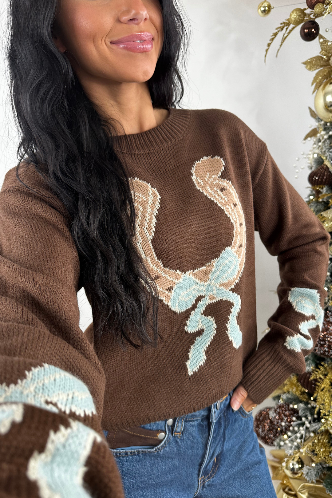 Woman wearing a brown sweater with decorative horseshoe in front of a decorated Christmas tree.