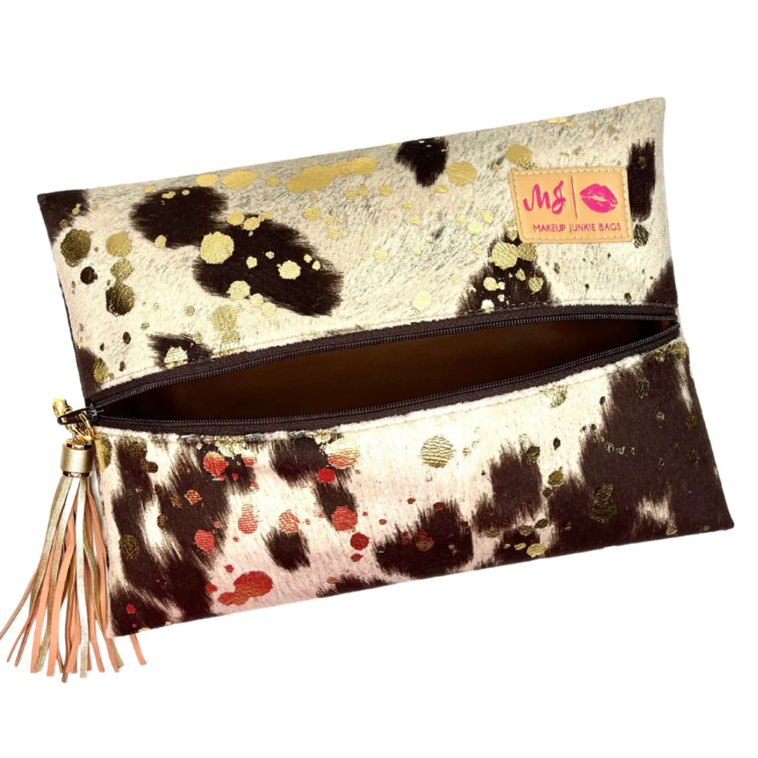 Front view of Rancher’s Daughter travel bag in brown and white vegan cowhide print with acid-wash, dark brown zipper and matching tassel.