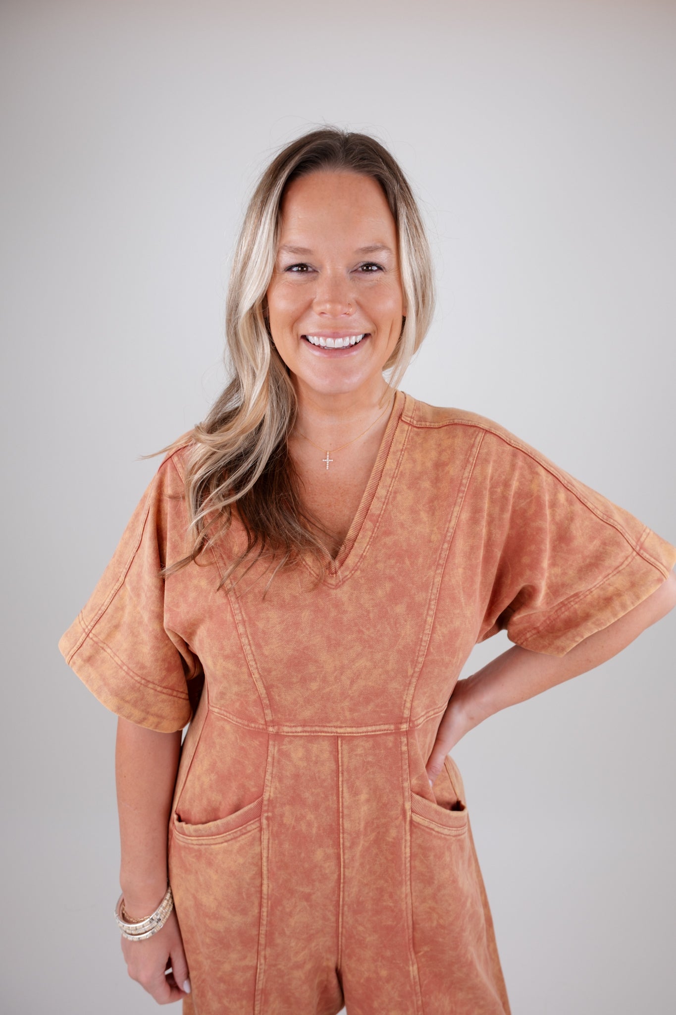 Woman wearing a rust colored jumpsuit against a plain background
