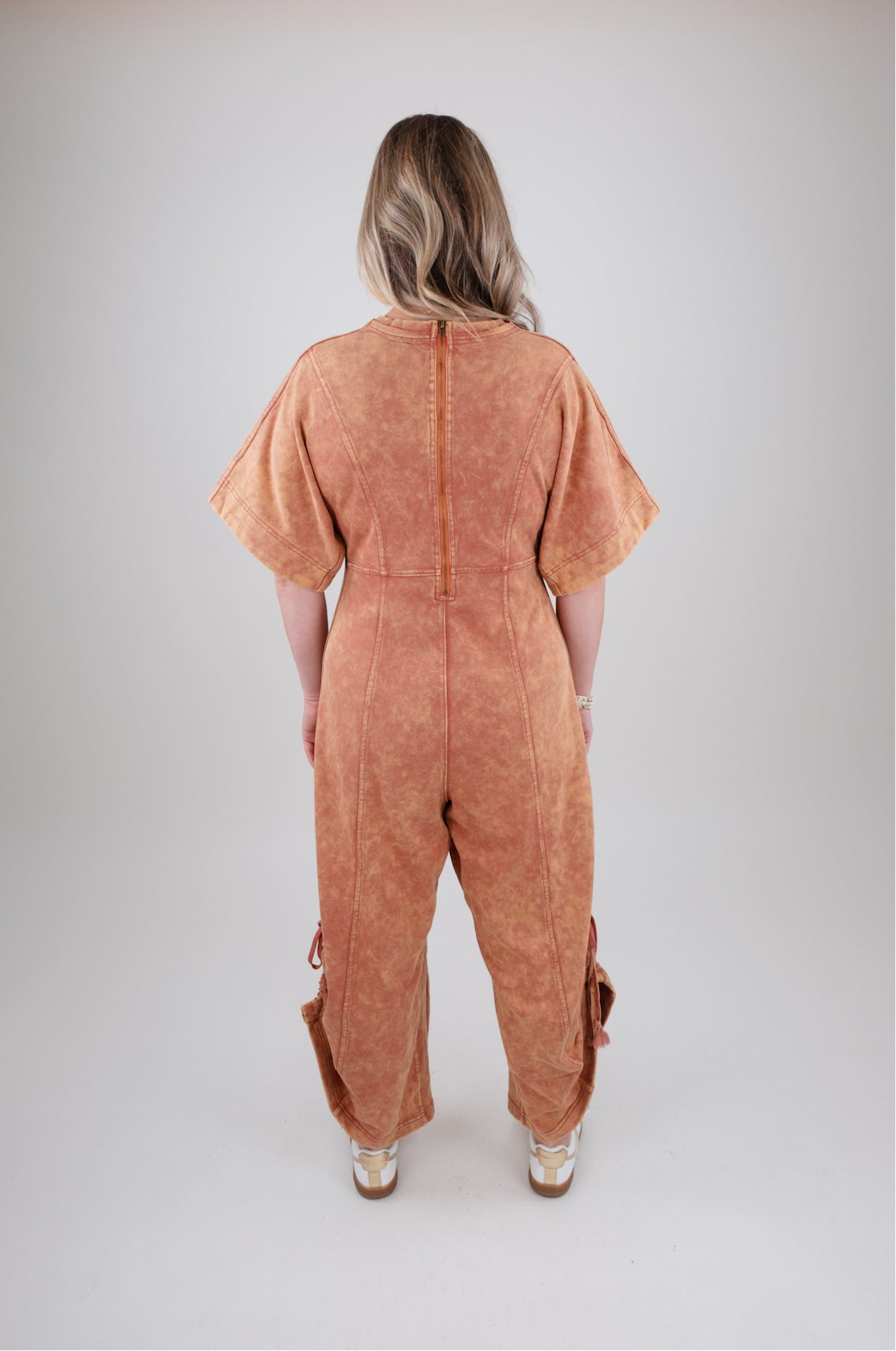 Person wearing a rust colored jumpsuit on a plain background