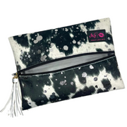 Front view of Rodeo Queen Makeup Junkie Bag with black‑and‑white vegan cowhide print, acid‑wash sparkle, black zipper and tassel.