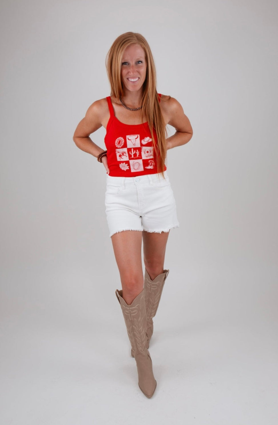 Woman wearing a red tank top with white patterns and white shorts, standing against a plain background.