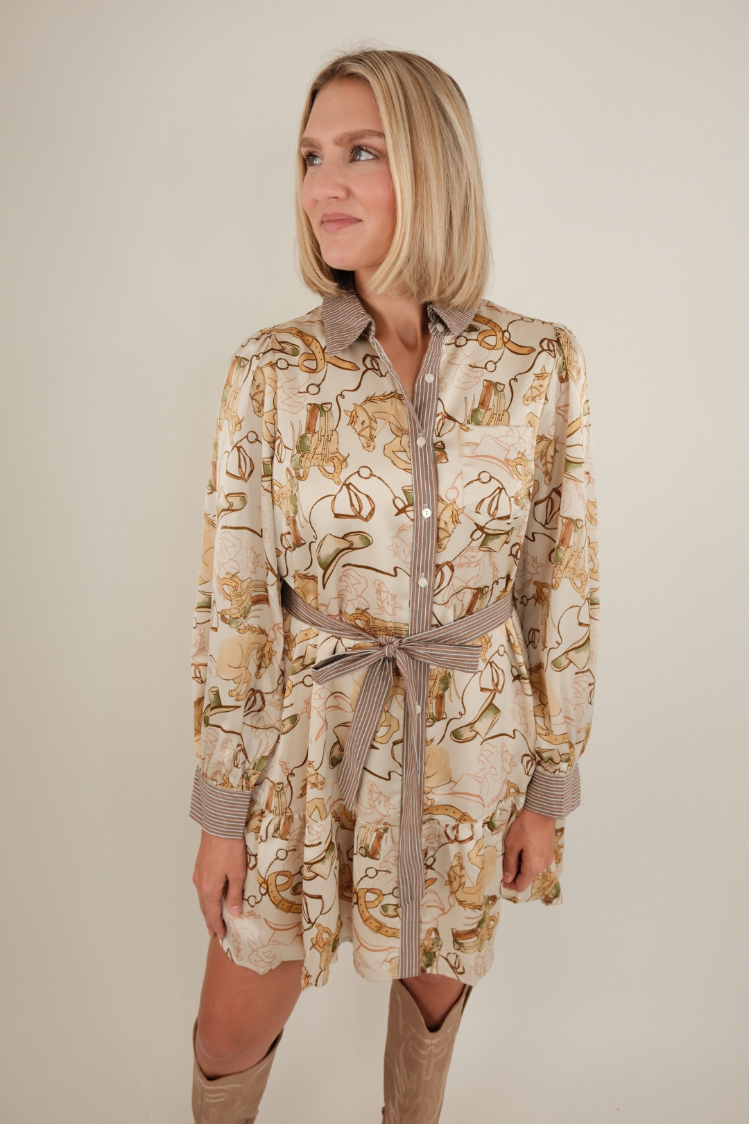 Close-up of ivory Rodeo Rendezvous Mini Dress highlighting bridle and horse print details, striped button placket, and sash belt.
