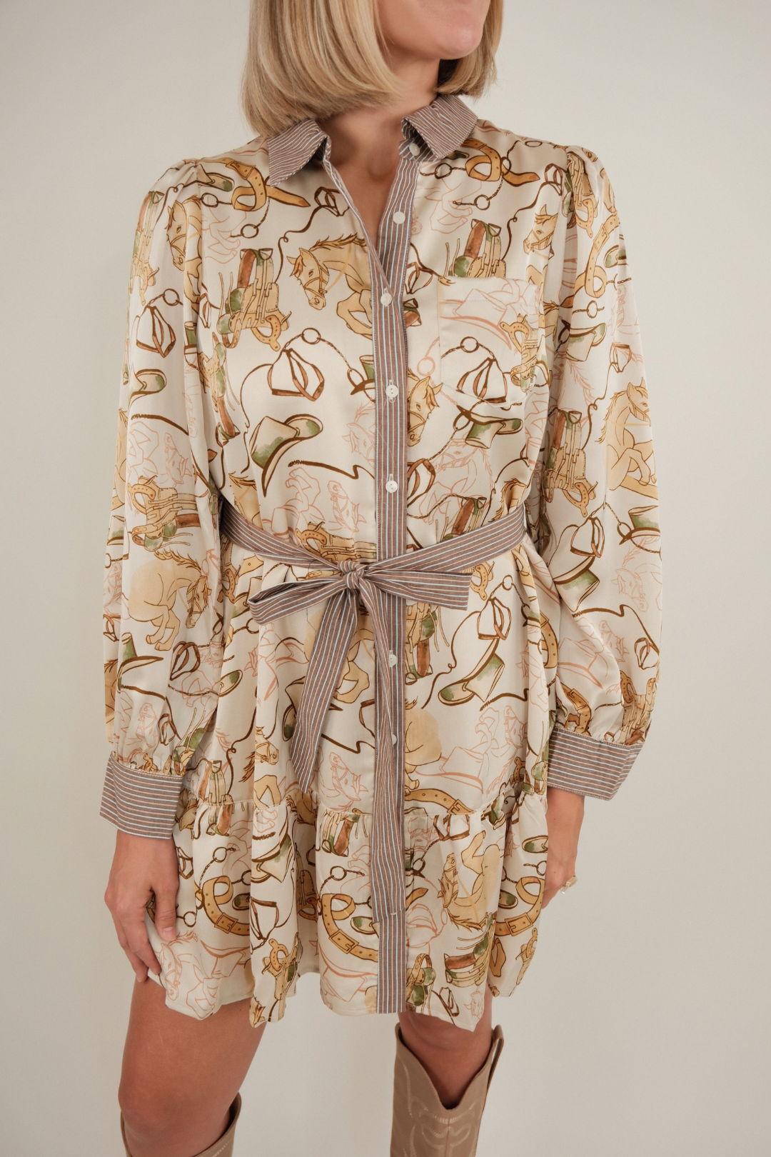 Full body shot of model in ivory Rodeo Rendezvous Mini Dress styled with boots, equestrian print dress with ruffle hem and puff sleeves.