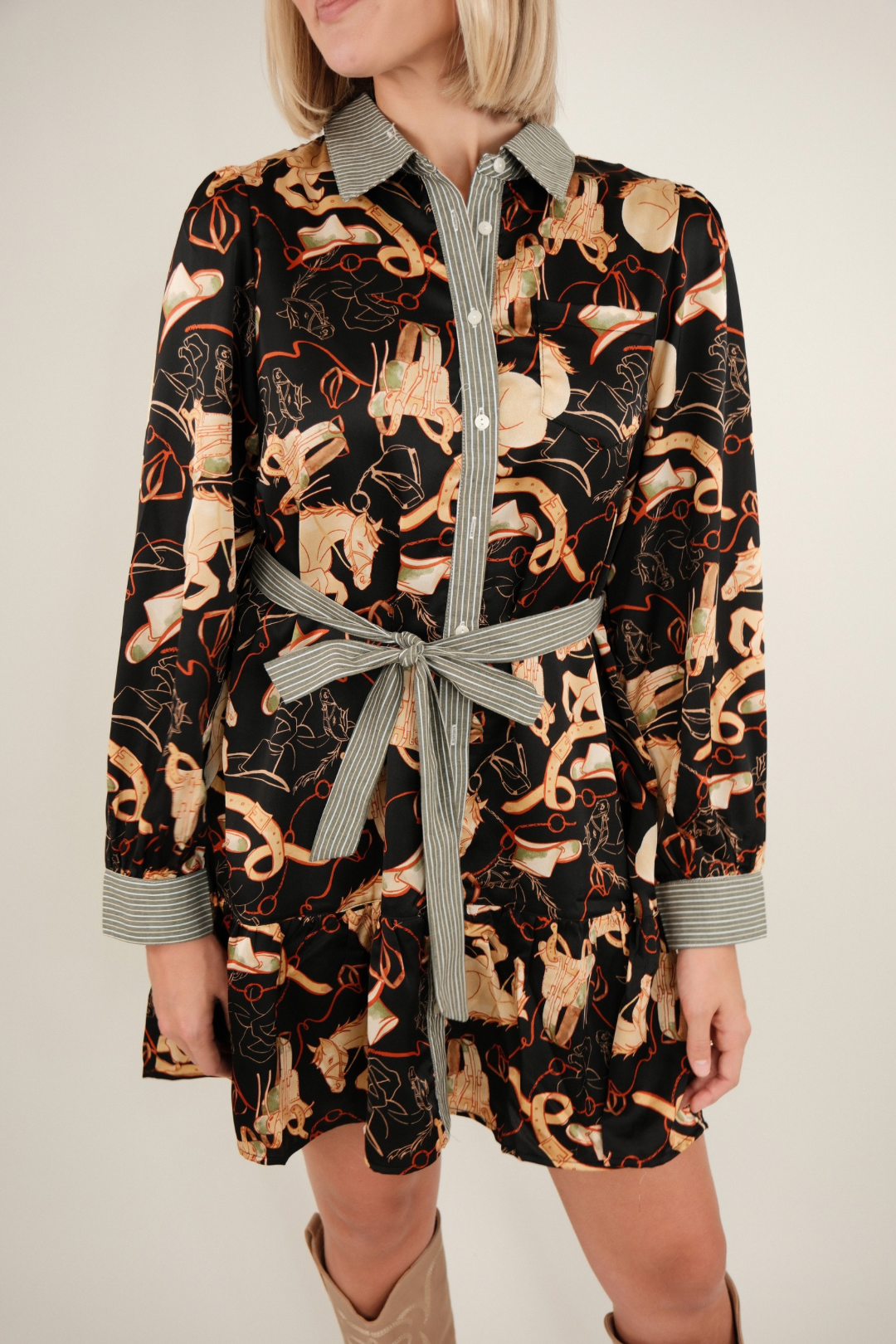 Full body shot of model wearing black Rodeo Rendezvous Mini Dress styled with cowboy boots, bold equestrian western mini dress.