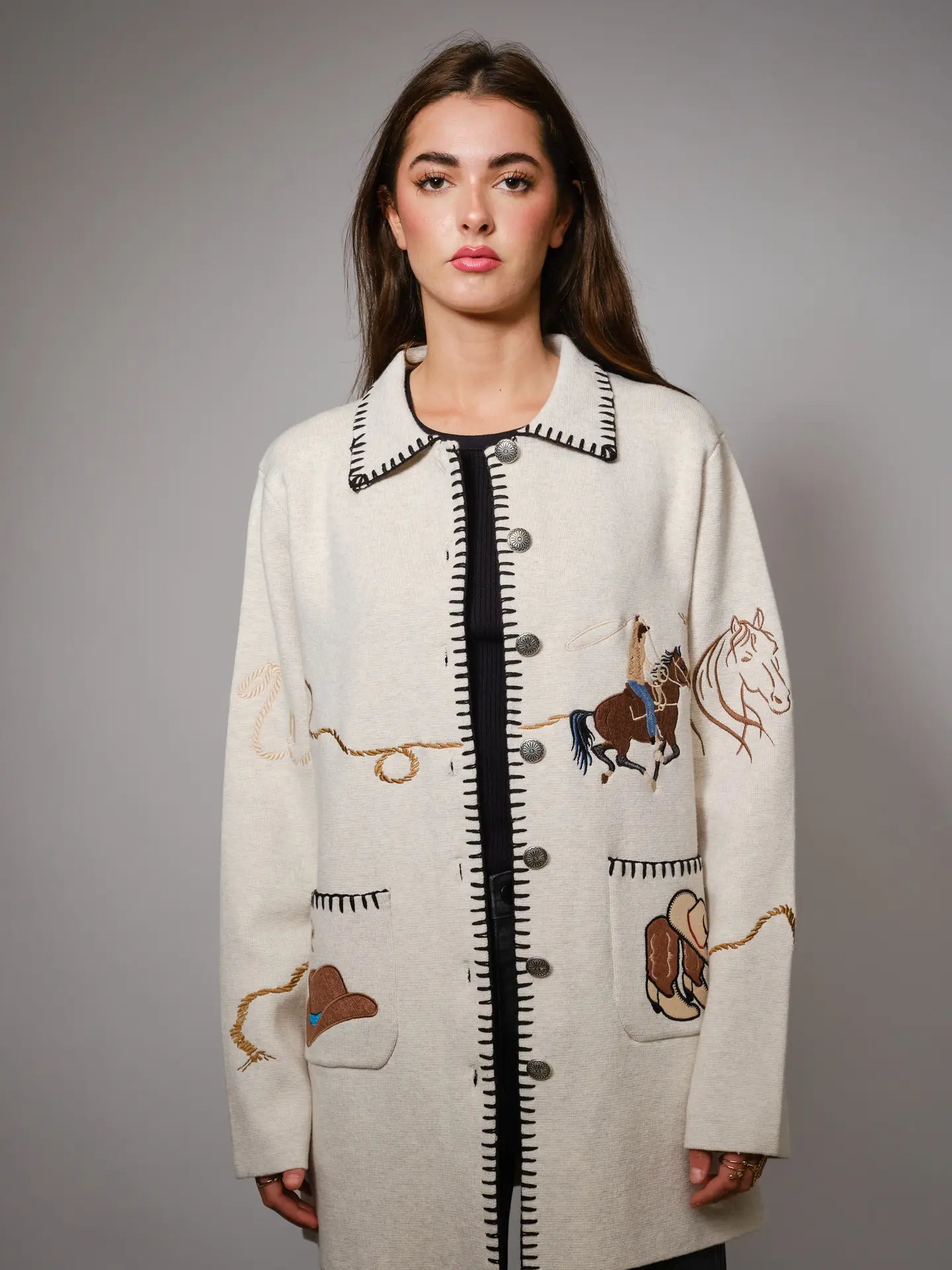 Woman wearing a cream-colored coat with embroidered western designs on a gray background