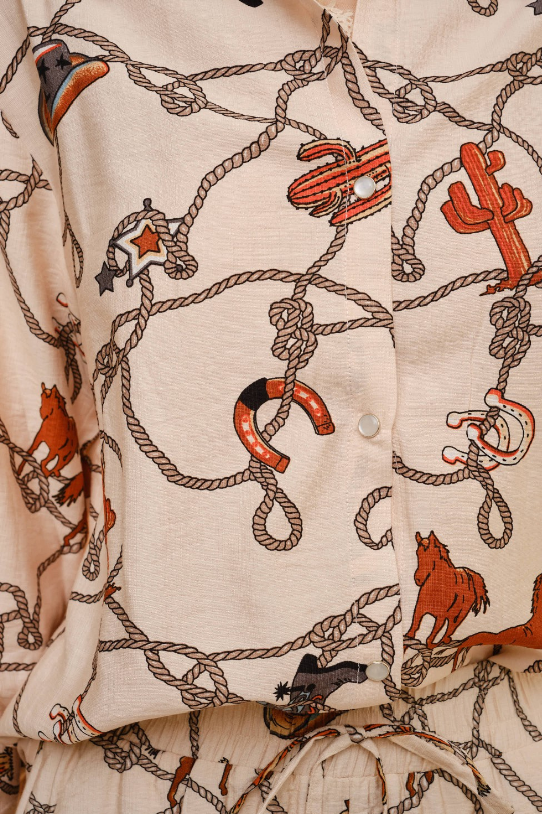 Shirt with western-themed pattern featuring horses, ropes, and cacti on a beige background.