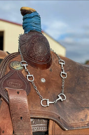 Close-up of a silver bit necklace over the horn of a horse saddle.