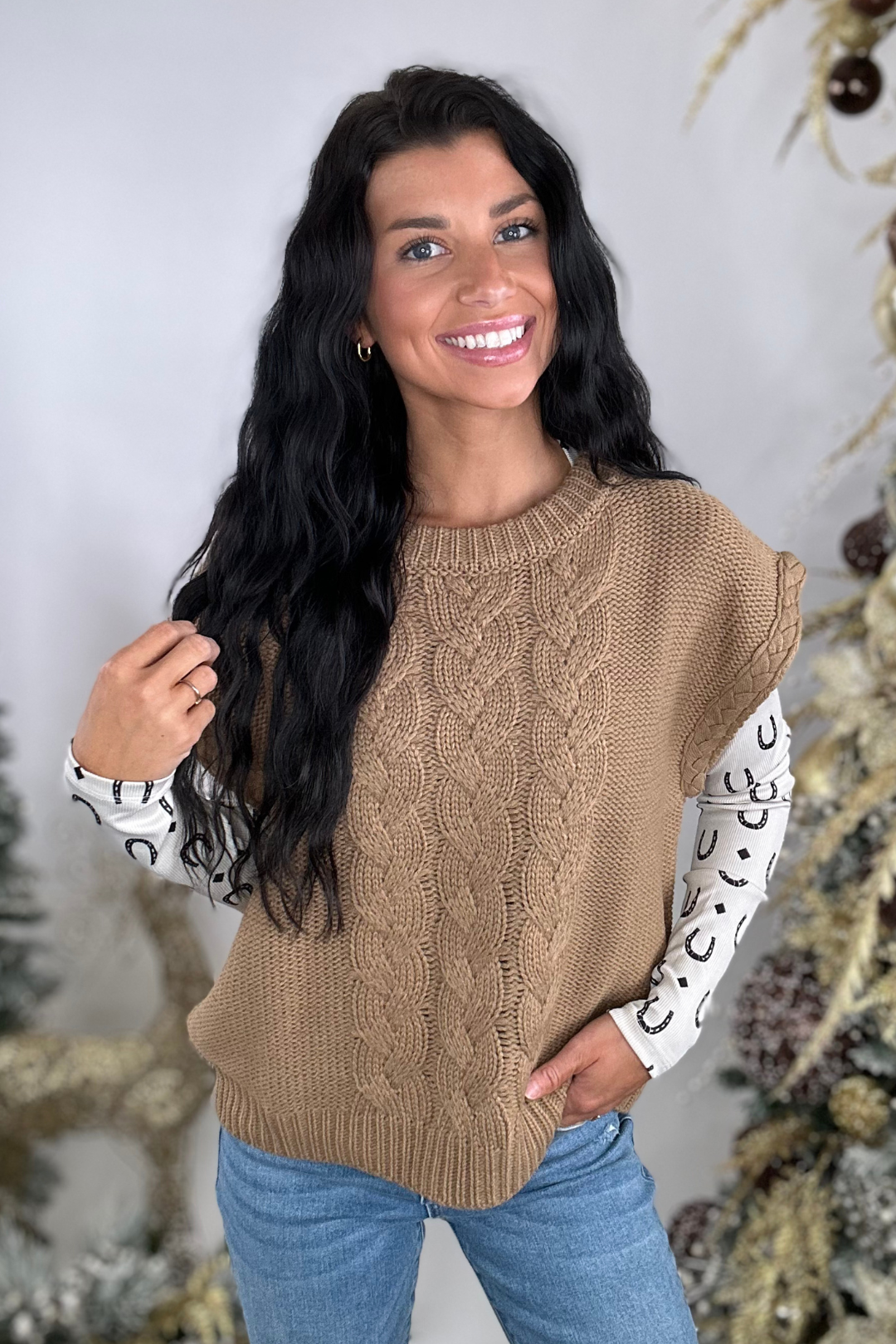 Woman wearing a brown cable knit sweater with patterned sleeves against a neutral background