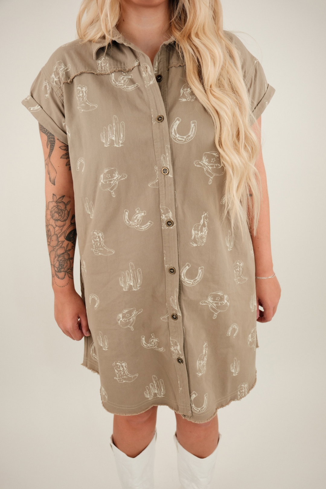 Model wearing boxy-fit Saddle Sketch shirt dress in taupe with button-down front and white western sketches of boots, cacti, and horseshoes.