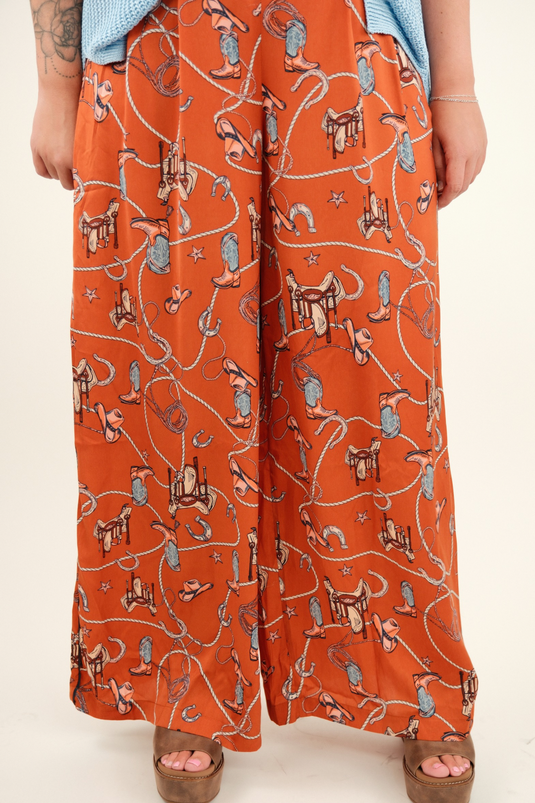 Rust orange silky wide-leg trousers with a high waist and vintage western print of boots, saddles, ropes, and stars.