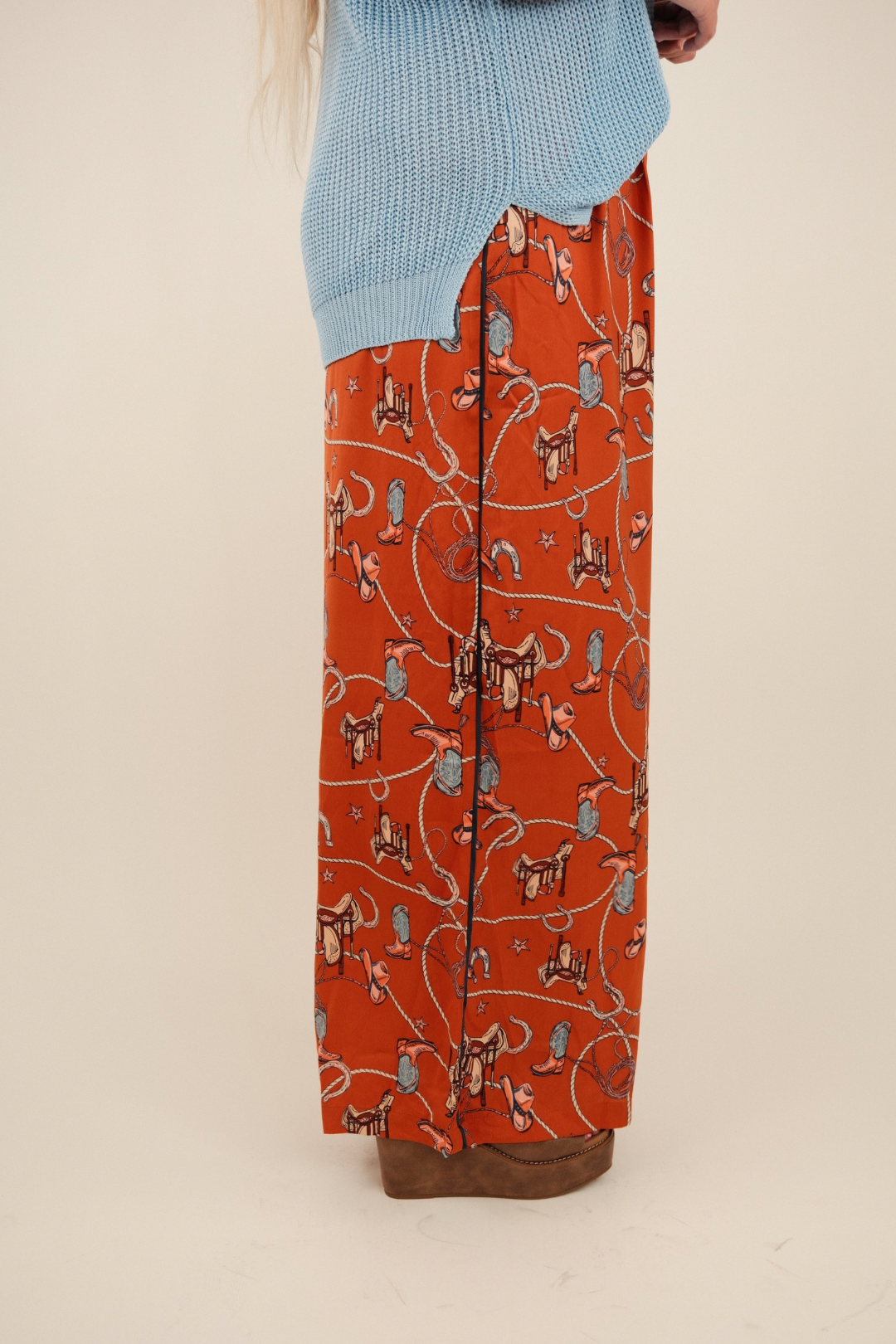 Rust orange silky wide-leg trousers with a high waist and vintage western print of boots, saddles, ropes, and stars.