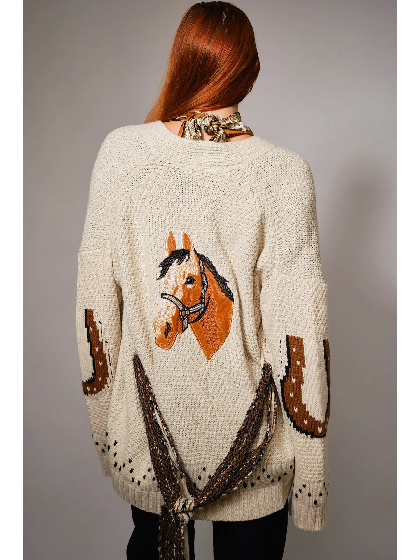 Back view of a person wearing a cardigan with a horse design on the back against a gray background