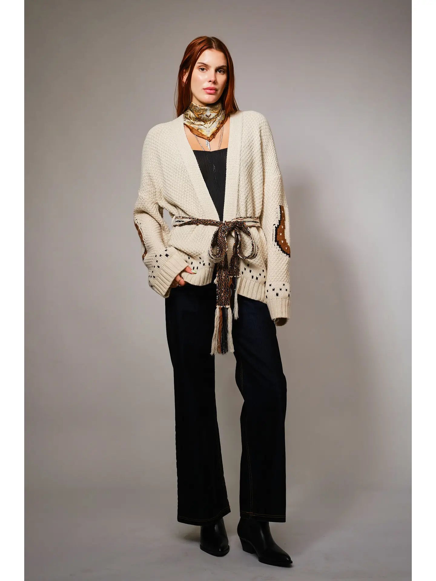 Woman wearing a beige cardigan with decorative elements on a plain background