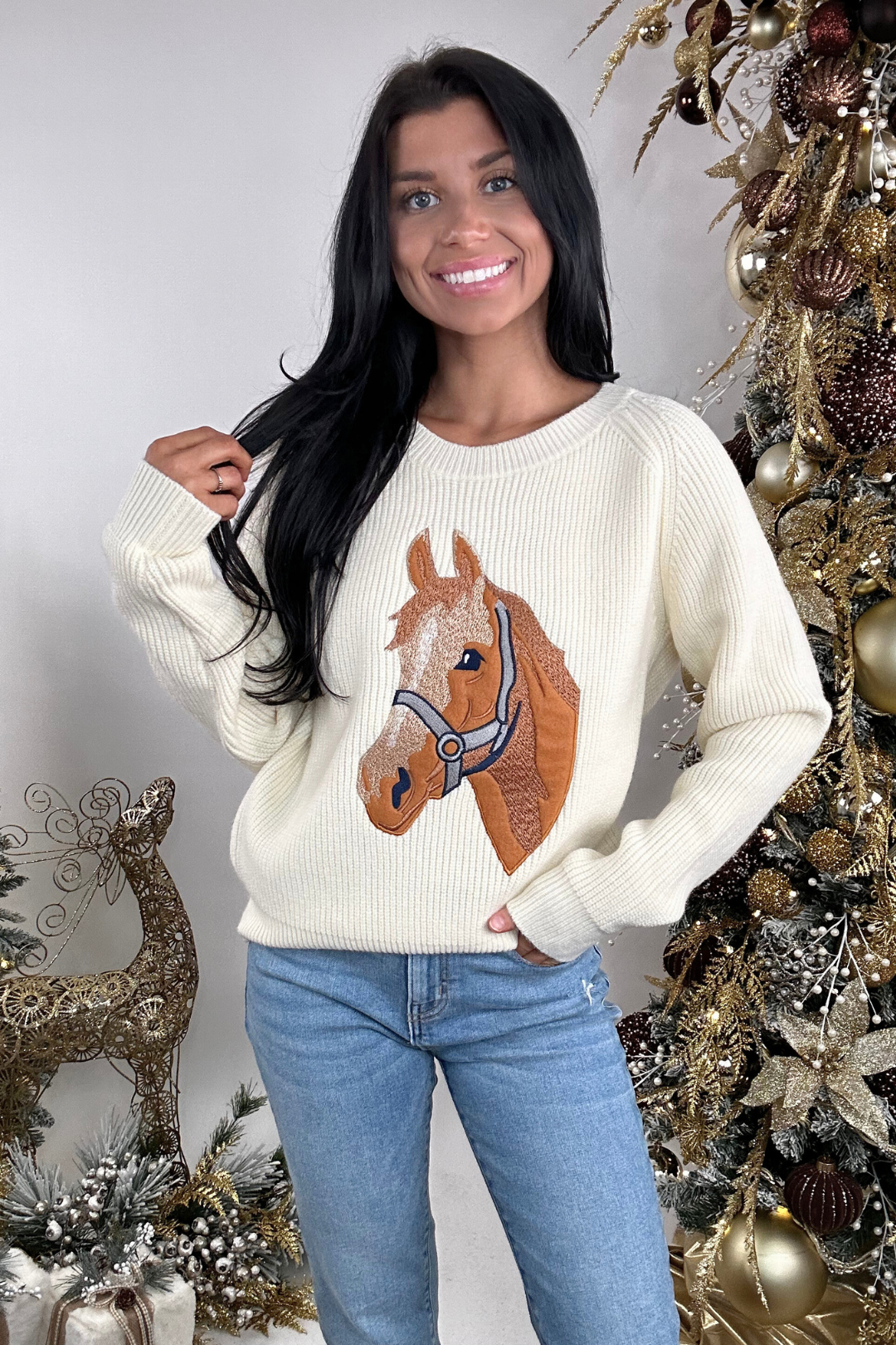 Woman wearing a sweater with a horse design in front of a decorated Christmas tree.
