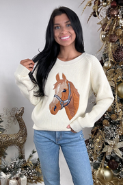 Woman wearing a sweater with a horse design in front of a decorated Christmas tree.