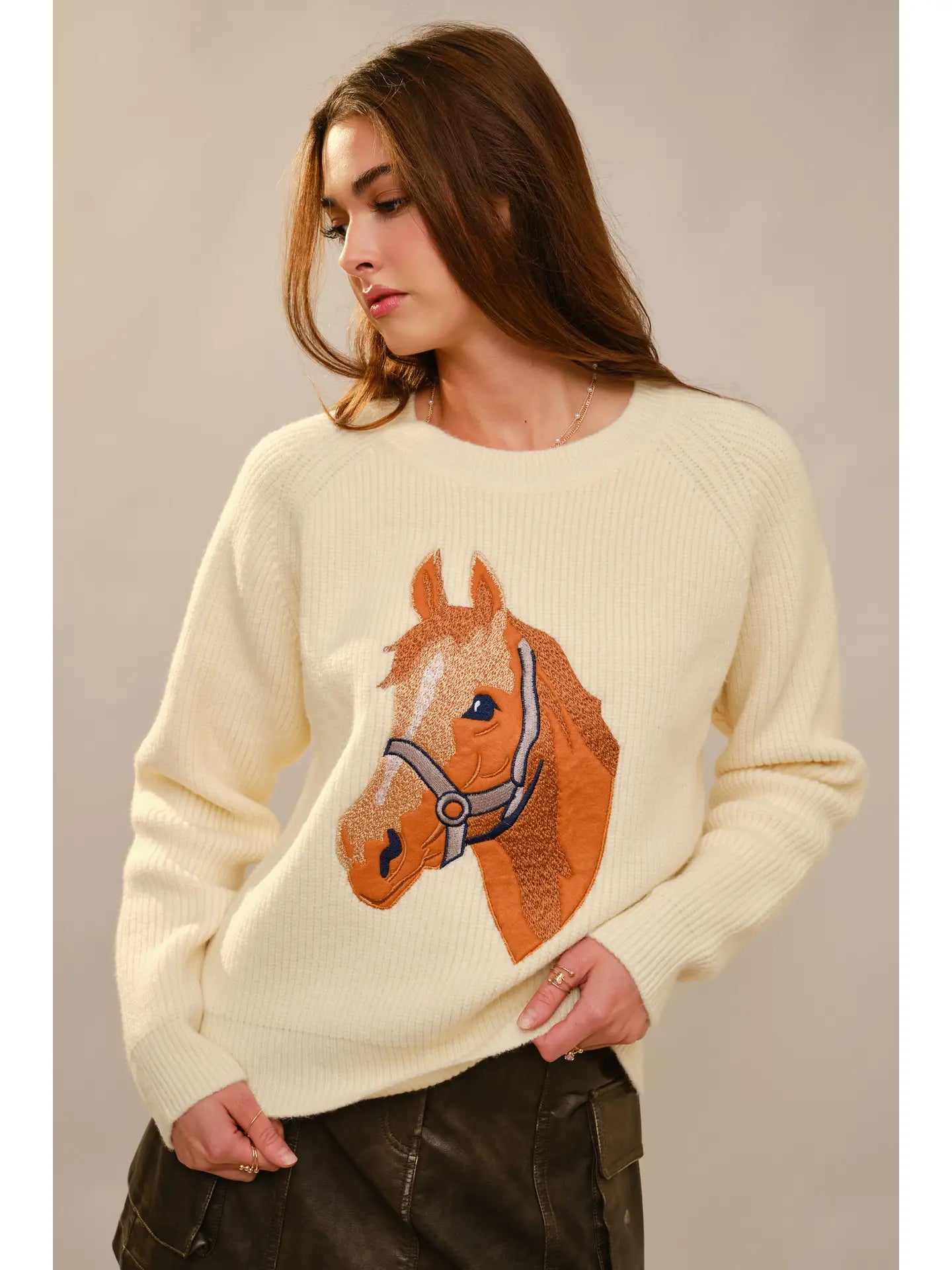Woman wearing a cream sweater with a horse design against a plain background