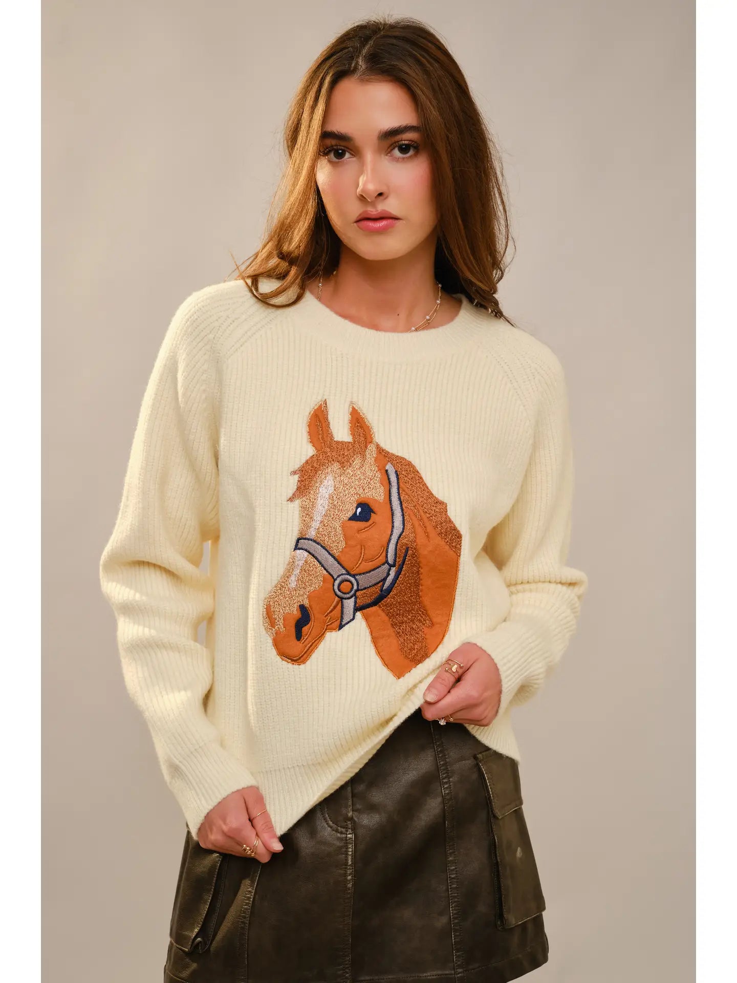 Woman wearing a cream sweater with a horse design against a plain background