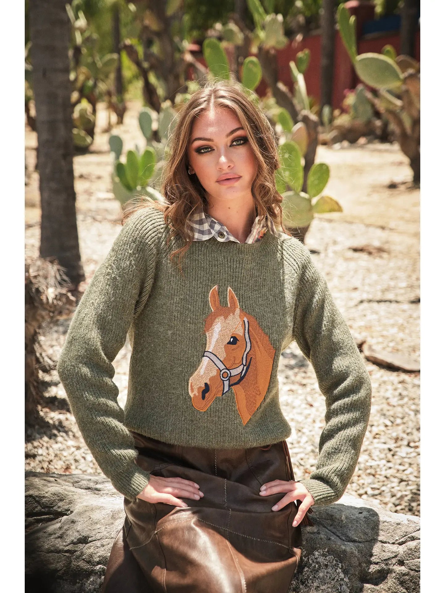 Woman wearing a green sweater with a horse design in an outdoor setting with cacti.
