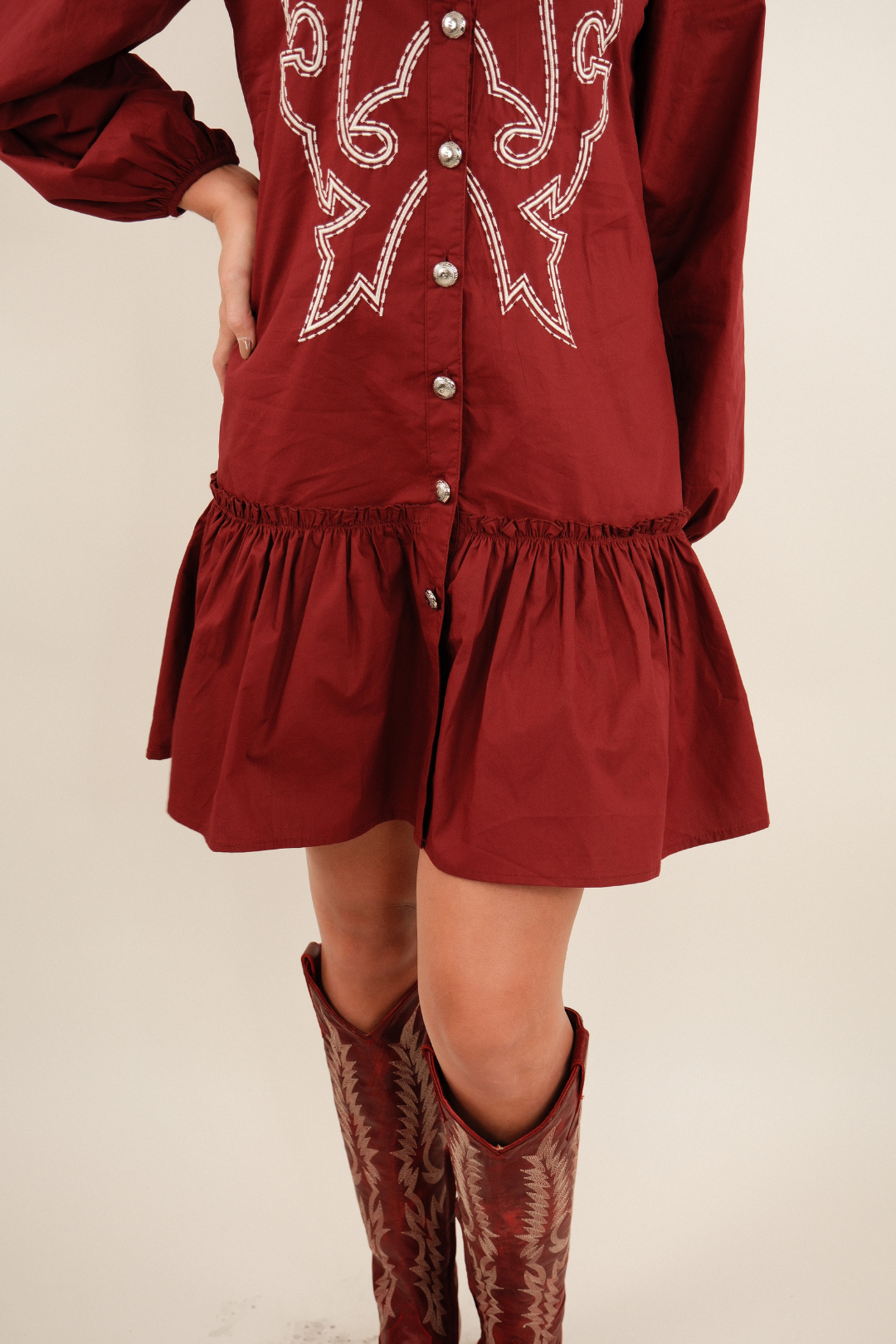 Close-up view of Saddle & Stitch Dress in burgundy showing concho button detail, peplum ruffle hem and relaxed fit.
