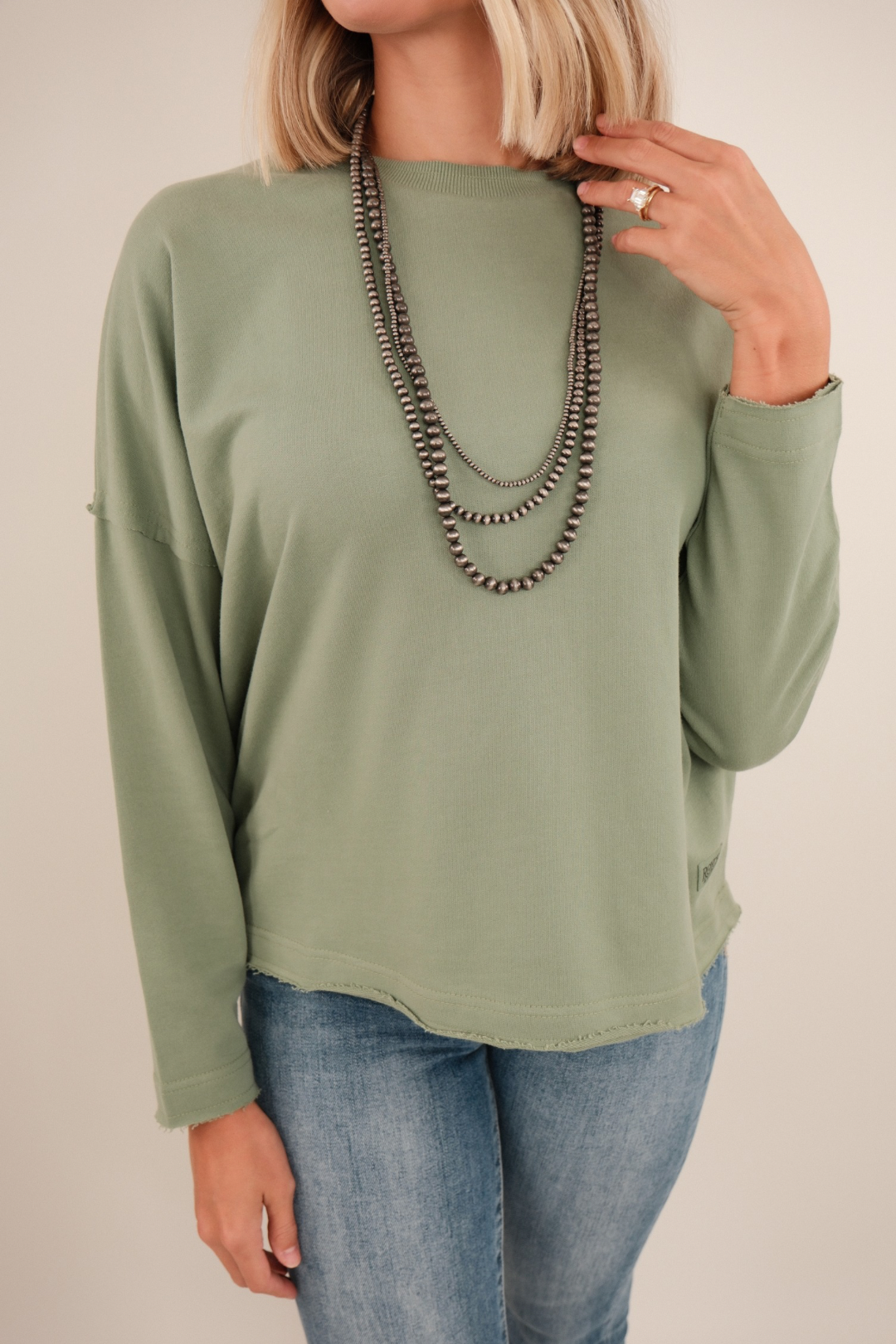 Close-up of women’s Sage Haven High Low Terry Top in sage green French terry highlighting raw-edge hem and soft textured fabric.