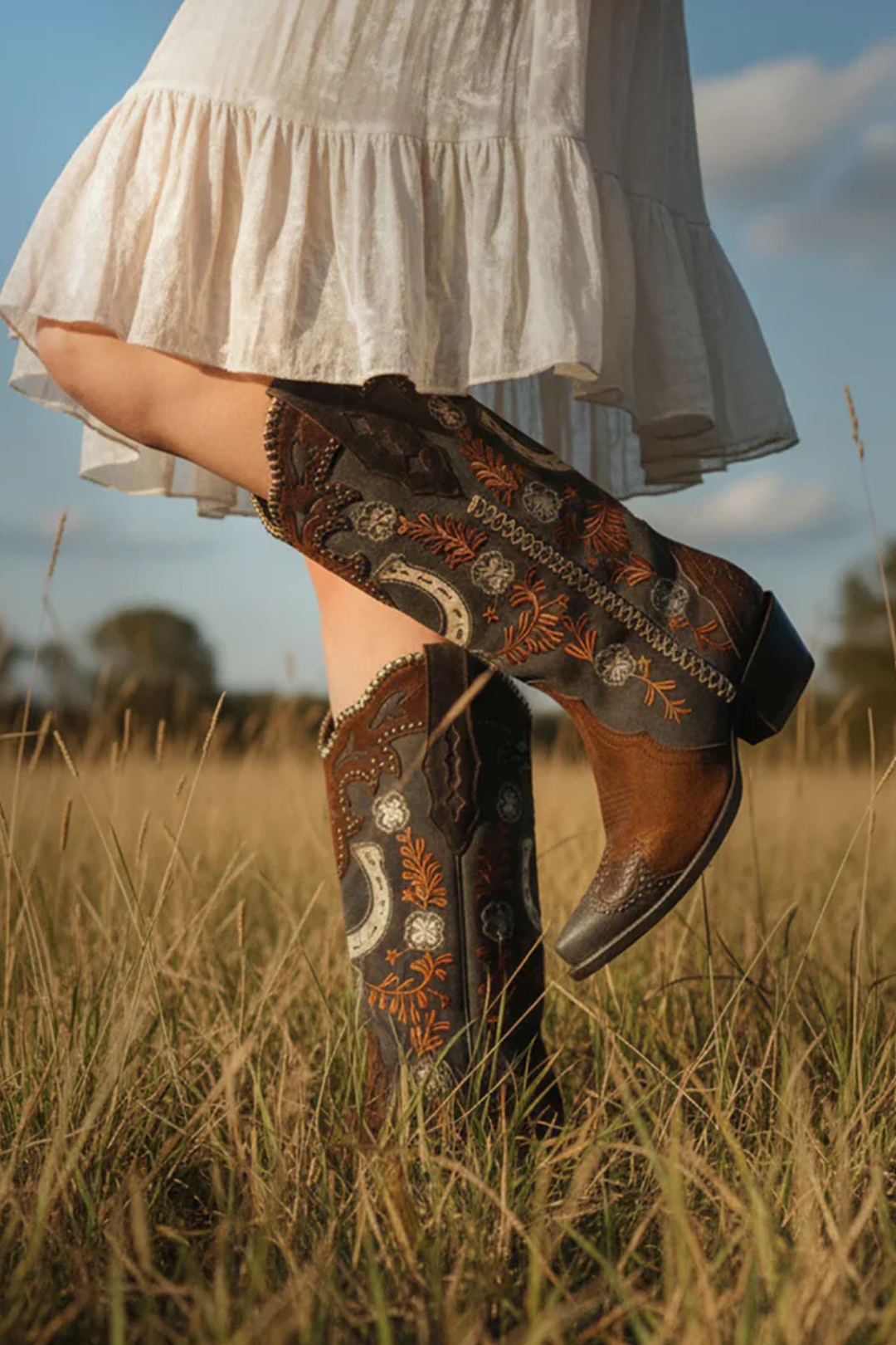 Person wearing embroidered boots in a field with a white dress.