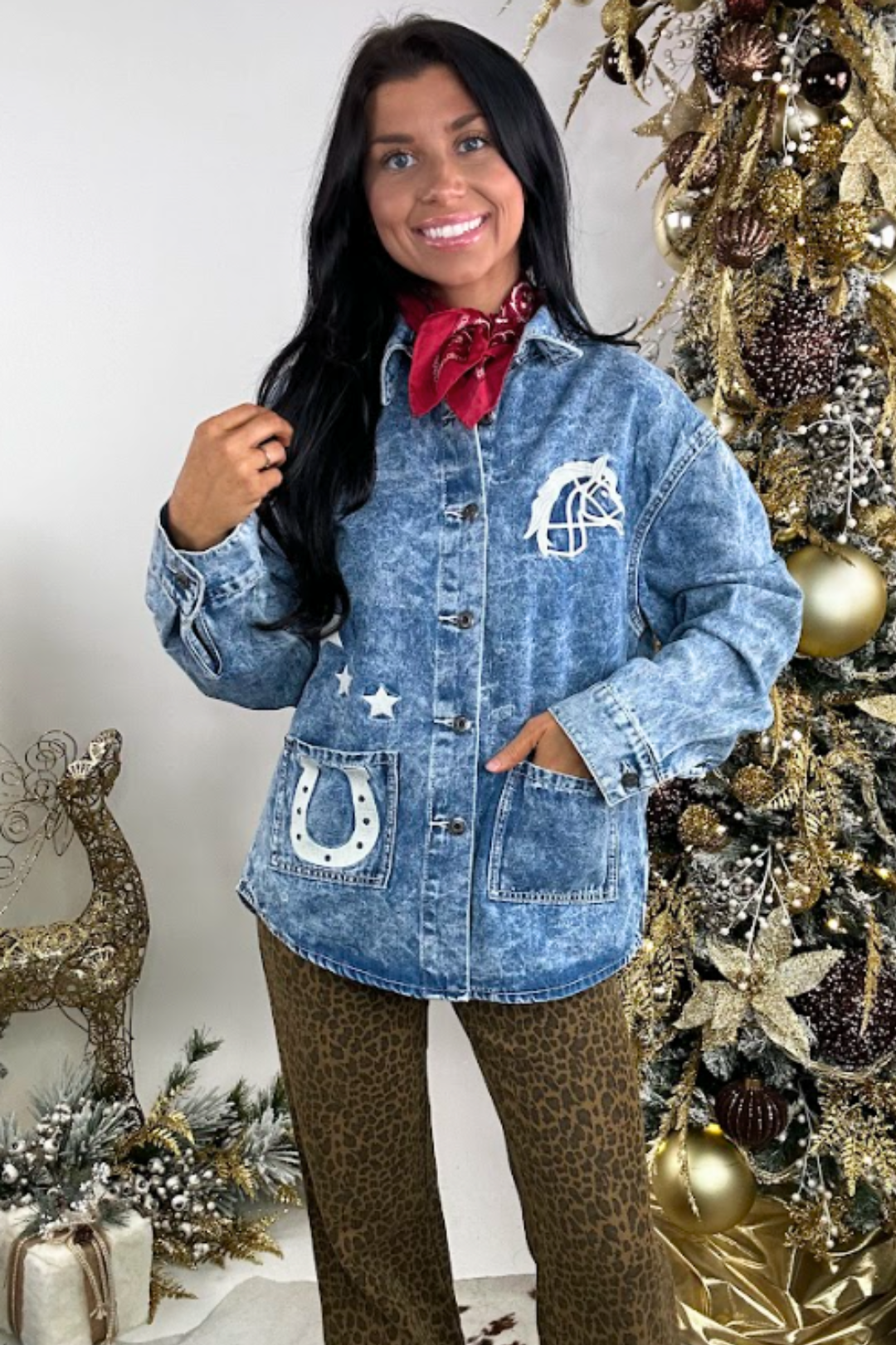 Woman wearing a denim jacket with horse shoe design in front of a decorated Christmas tree.
