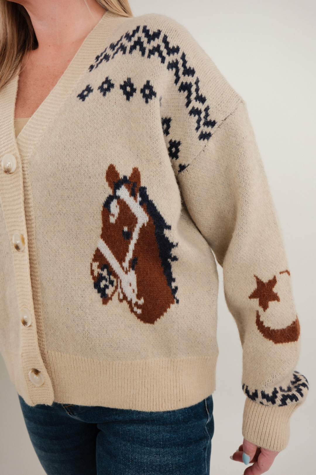 Close-up of women’s Starlight Mustang Cardigan in beige highlighting navy knit stitching, western horse motif and button detail.