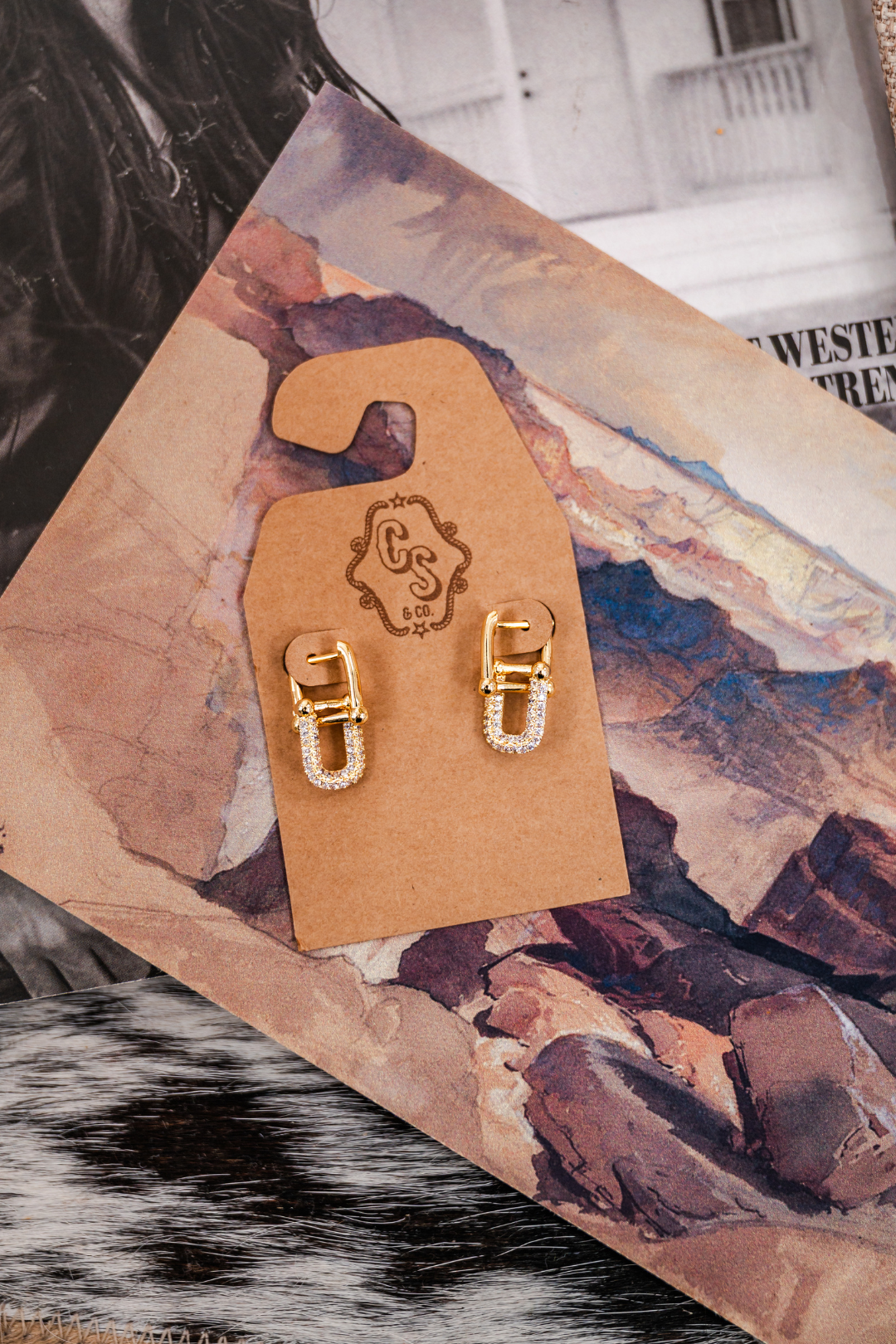 Gold hoop earrings on a wooden hook  displayed on a textured surface.