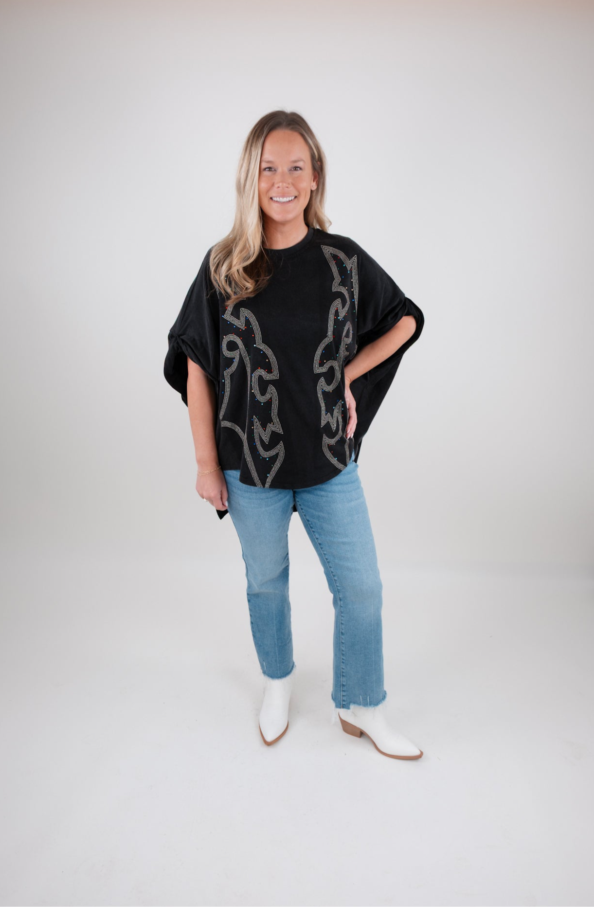 Woman wearing a black tunic with a boot stitch pattern, blue jeans, and white boots on a white background