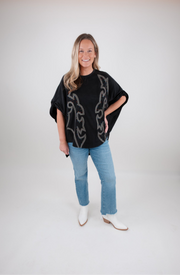 Woman wearing a black tunic with a boot stitch pattern, blue jeans, and white boots on a white background