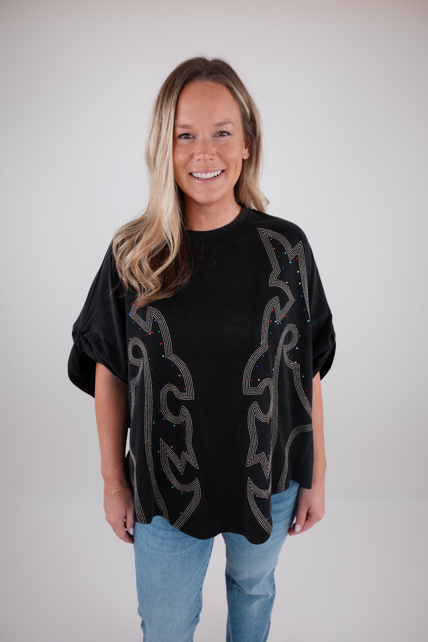 Woman wearing a black top with boot stitch patterns against a plain background