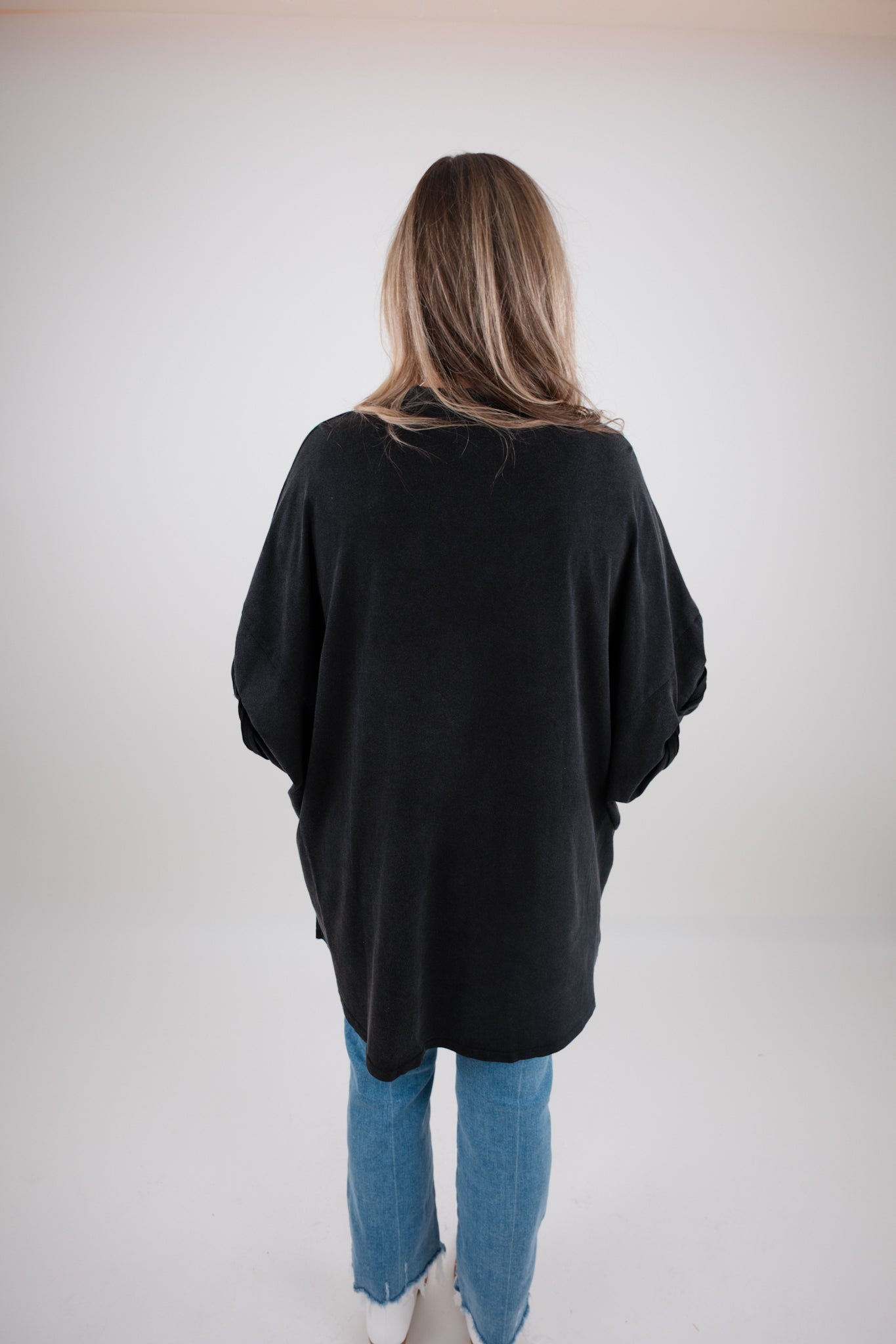 Person wearing a black oversized tunic and blue jeans against a plain background