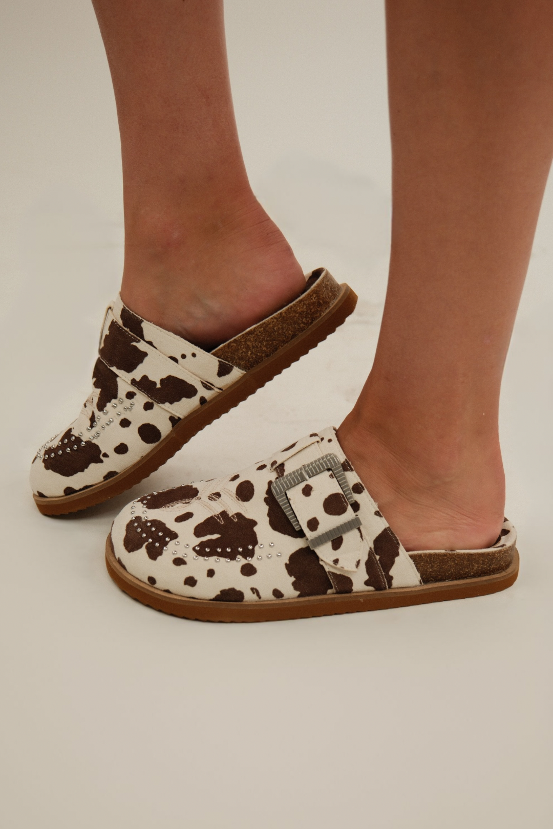 White & brown cow-print suede Studded Rodeo Slides with embroidered Western toe design and double row silver studs.
