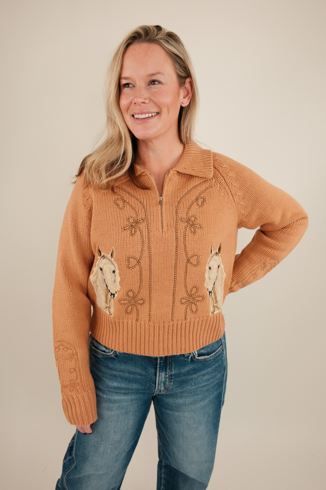Front view of Sundance Embroidered Quarter-Zip Sweater in light peach with floral embroidery, horse motif, mock neck, and bow-accented sleeves.