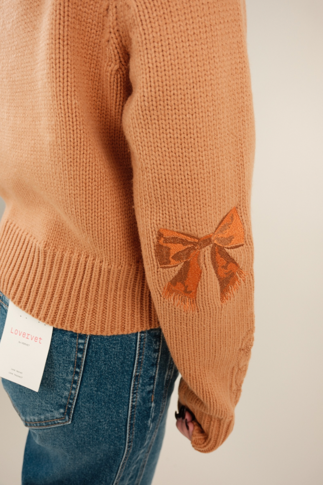 Side profile of Sundance Embroidered Quarter-Zip Sweater showing soft peach knit, embroidered detail, and feminine bow accents on elbows.