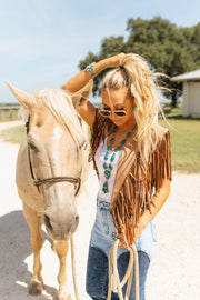 Woman in a fringe vest standing next to a horse outdoors