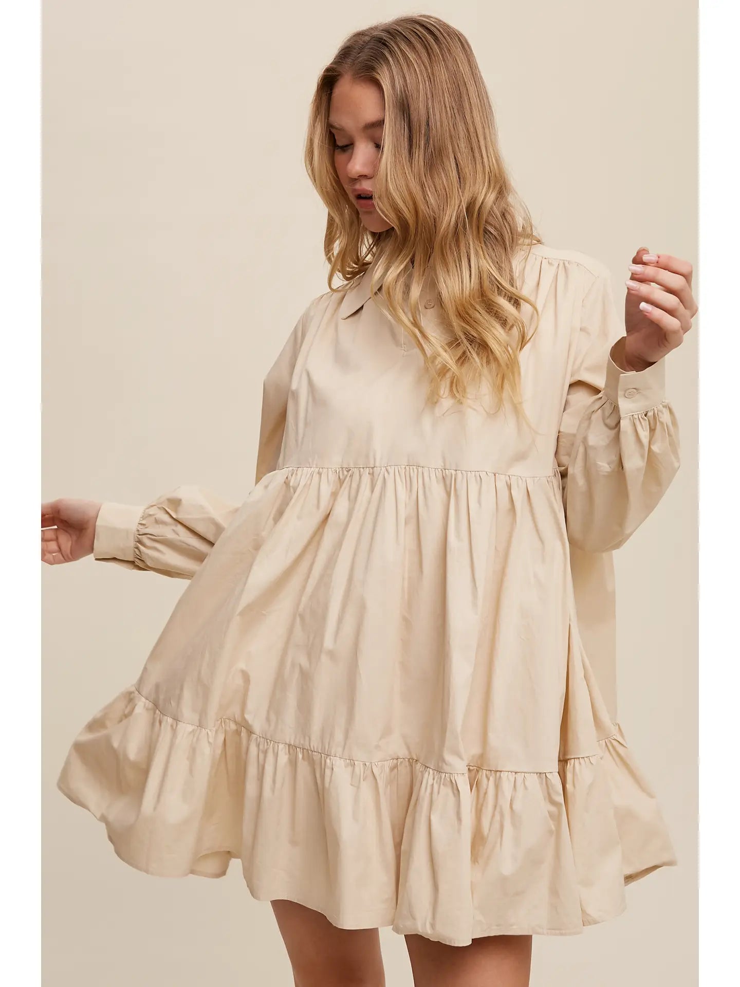 Woman wearing a beige dress with long sleeves against a plain background