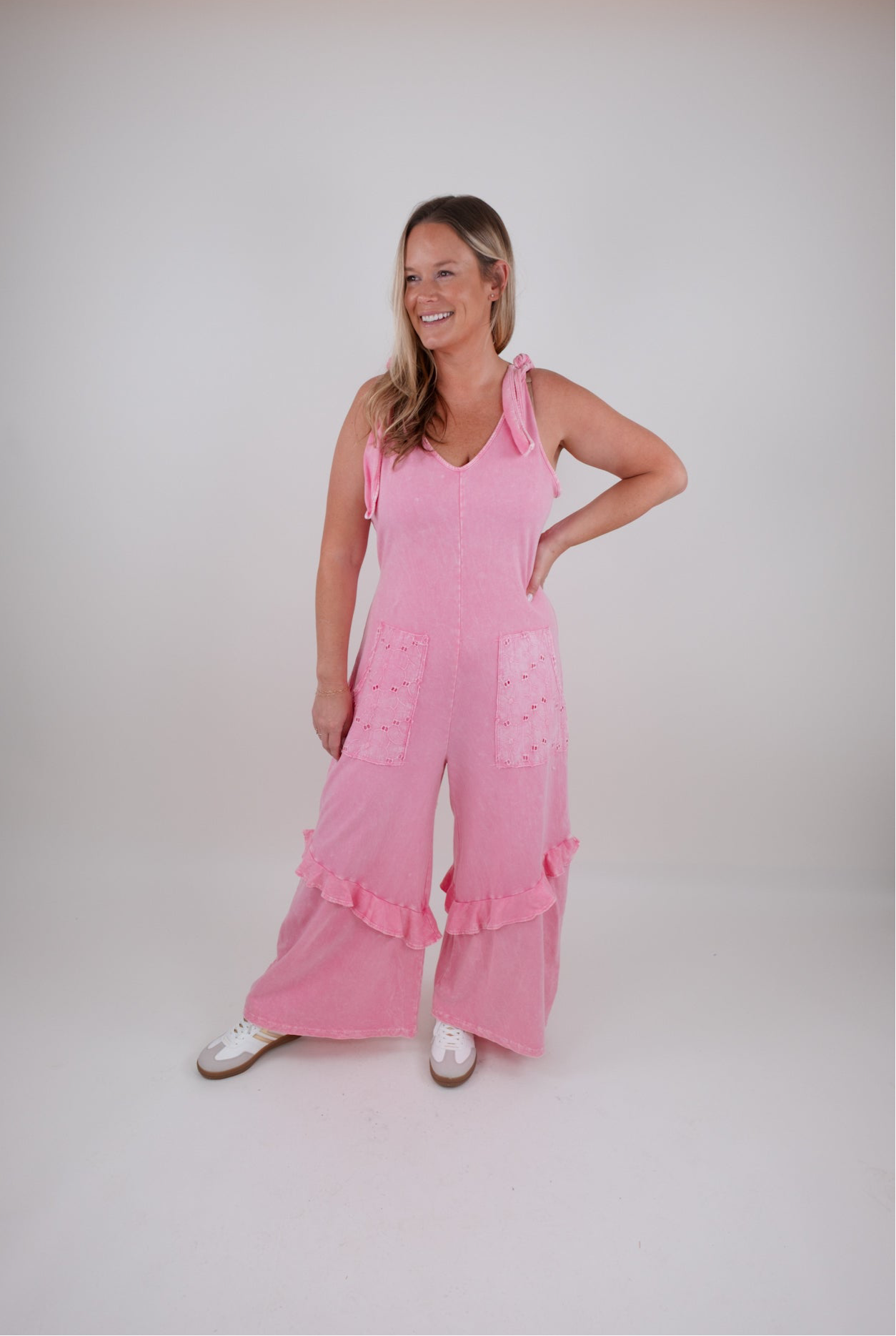 Woman wearing a pink jumpsuit with ruffled details on a white background