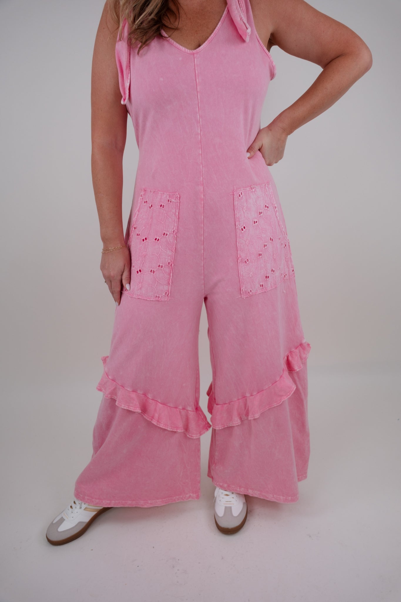 Person wearing a pink jumpsuit with ruffled details on a plain background
