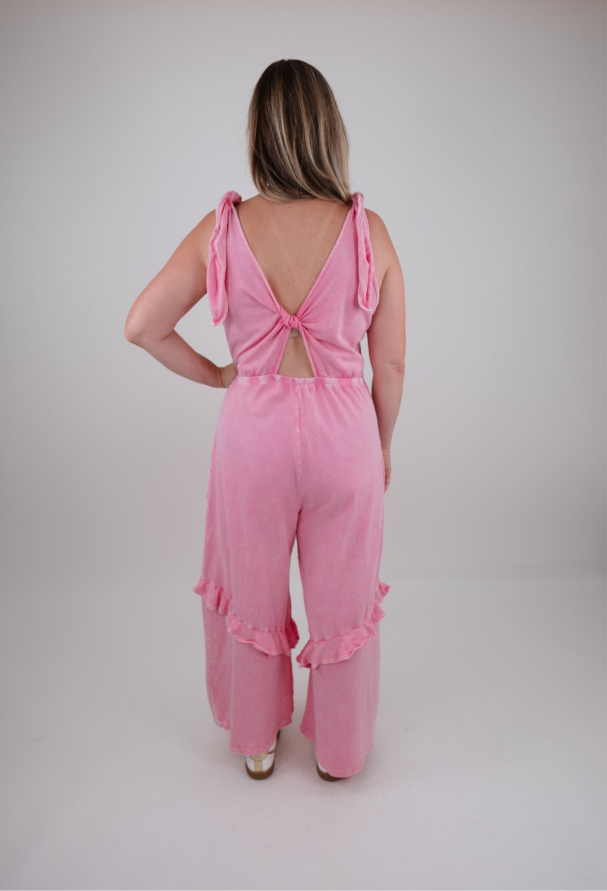 Woman wearing a pink jumpsuit with a back bow detail on a plain background