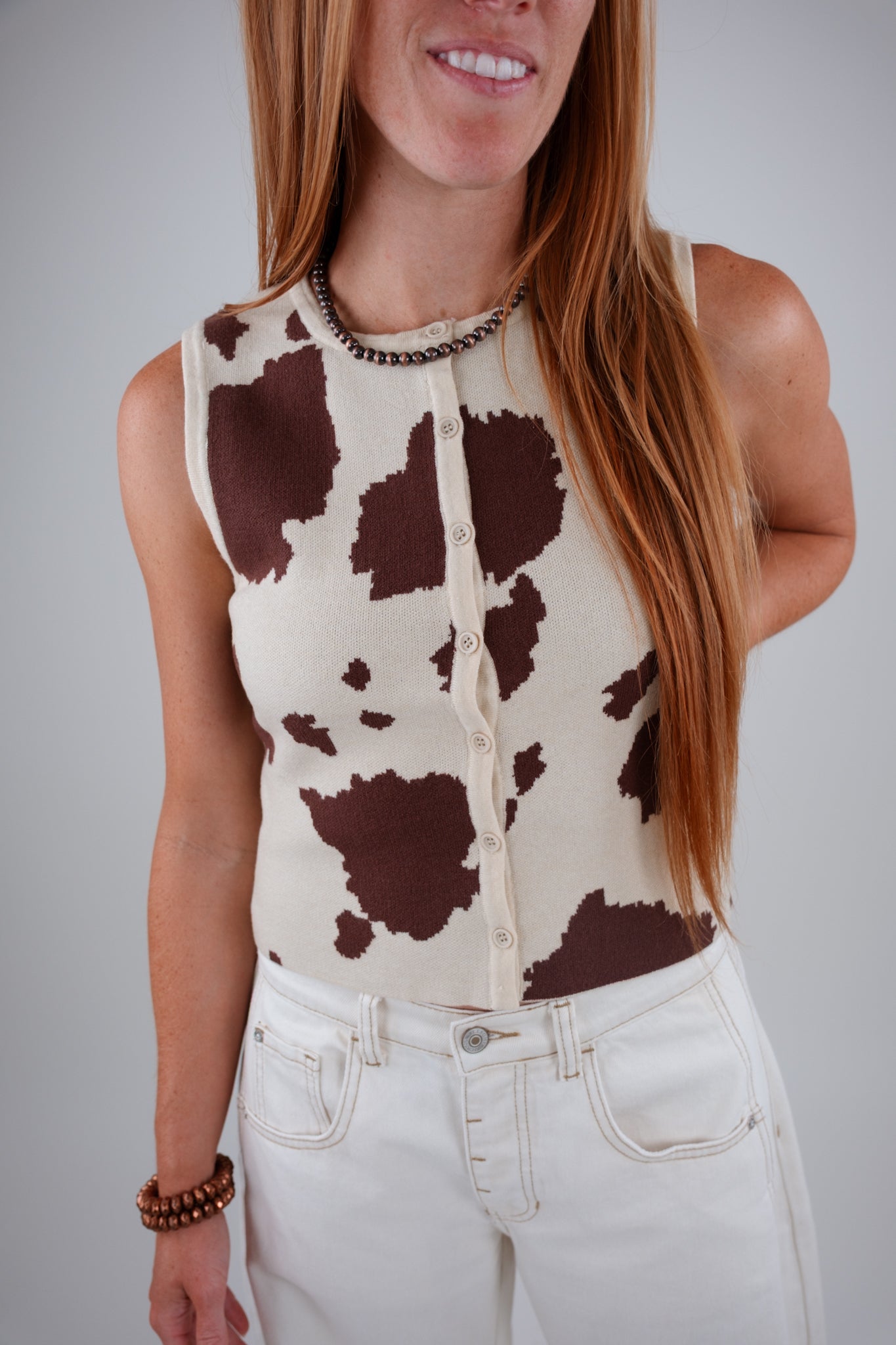 Person wearing a sleeveless cow print top and white pants against a plain background