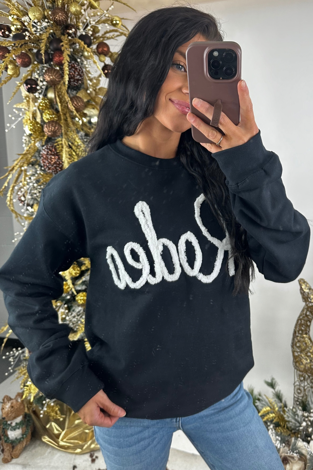 Person wearing a black sweatshirt with white "Rodeo" text, standing in front of a decorated Christmas tree.