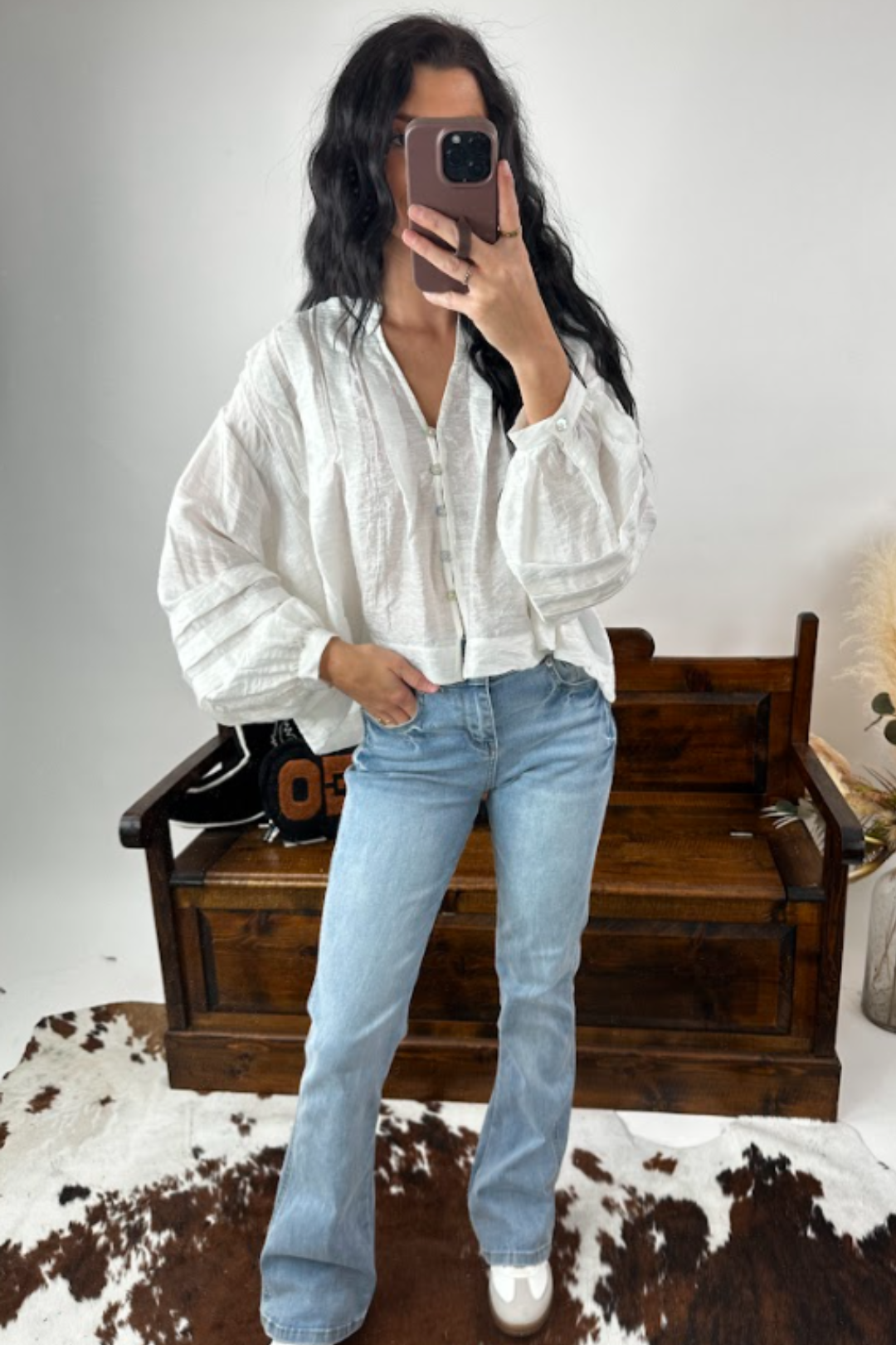 Person wearing a white shirt and light blue jeans sitting on a wooden bench.