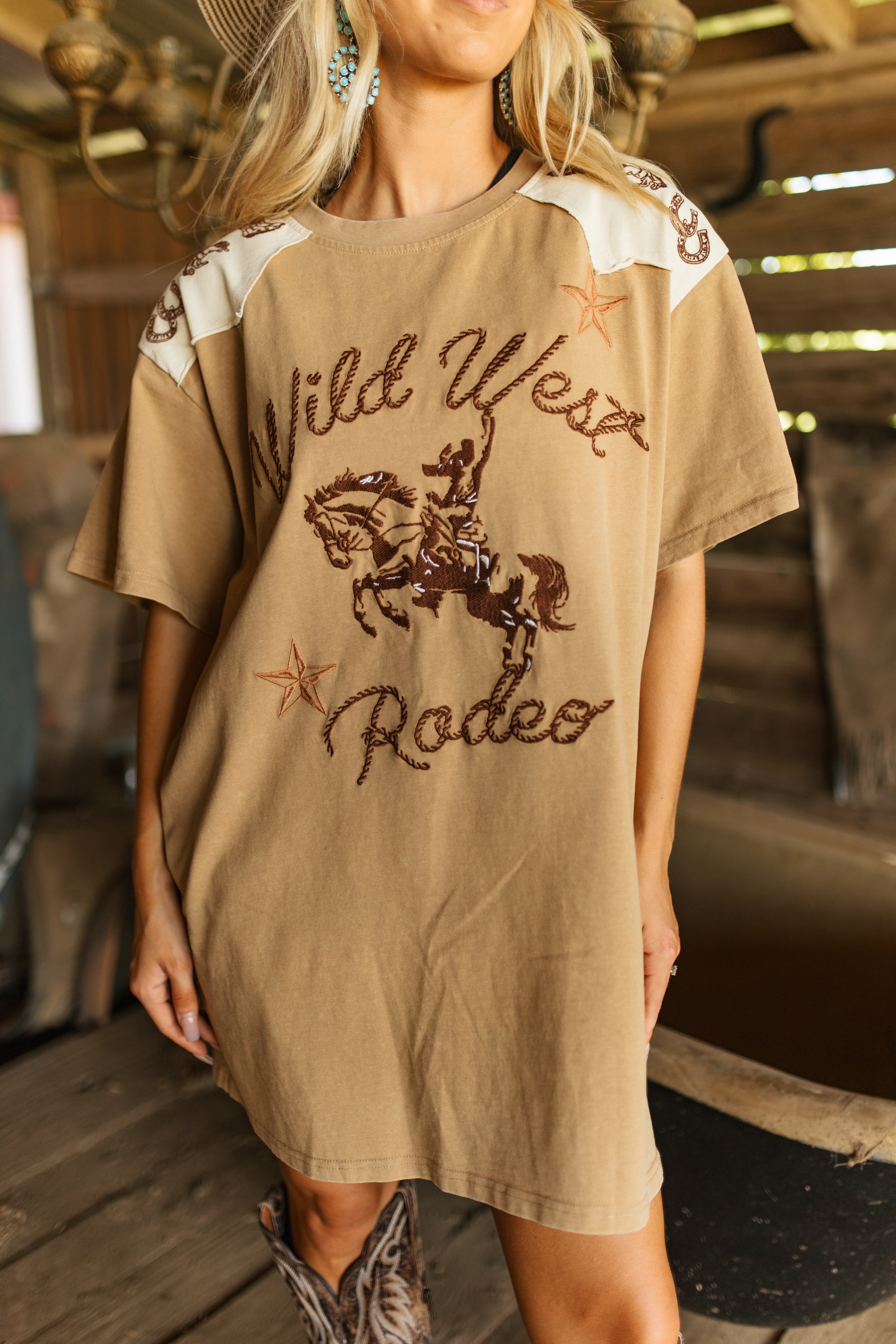 Person wearing a beige t-shirt with 'Wild West Rodeo' text and graphic indoors.