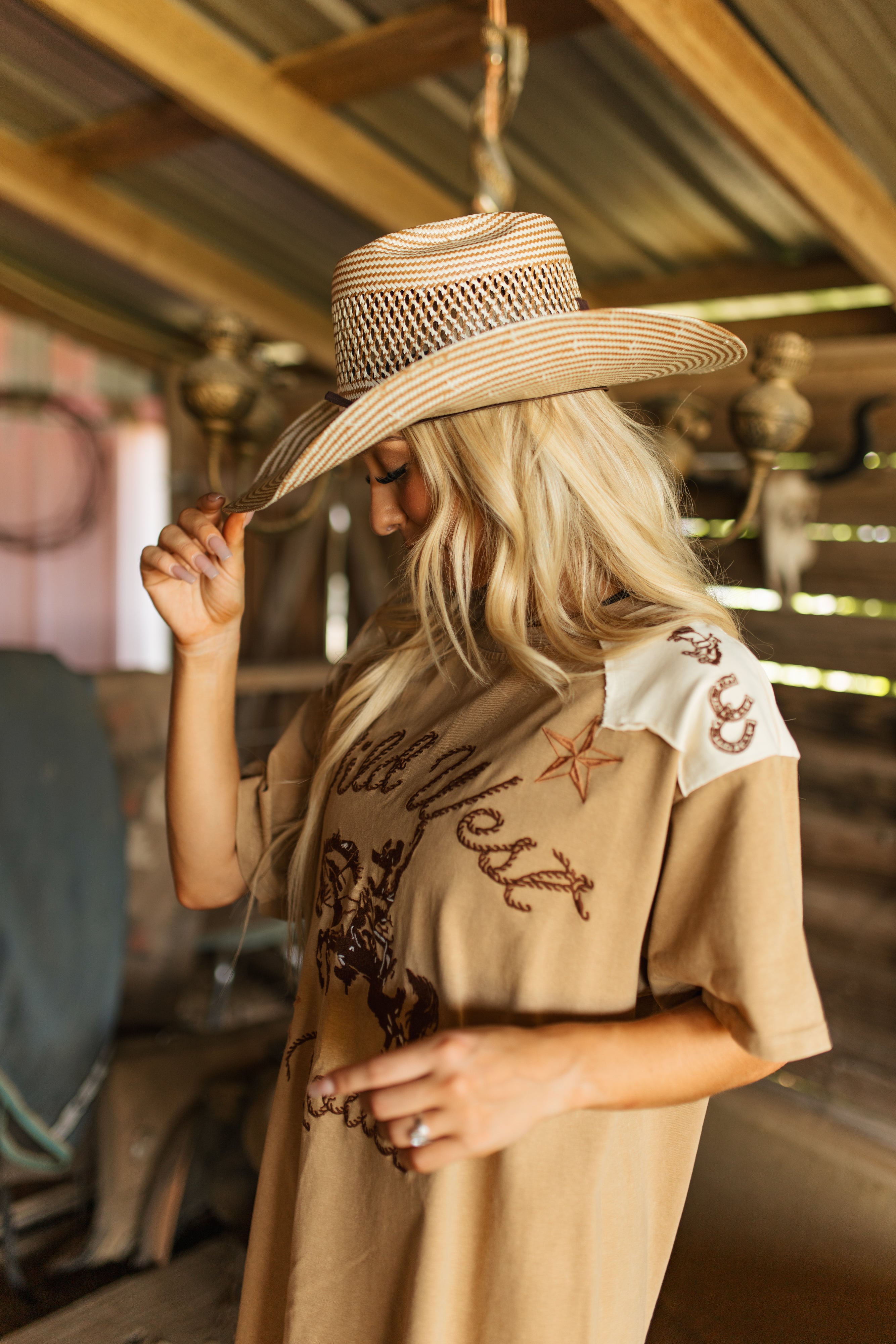 Person wearing a wide-brimmed hat and a beige shirt with western designs in an indoor setting.