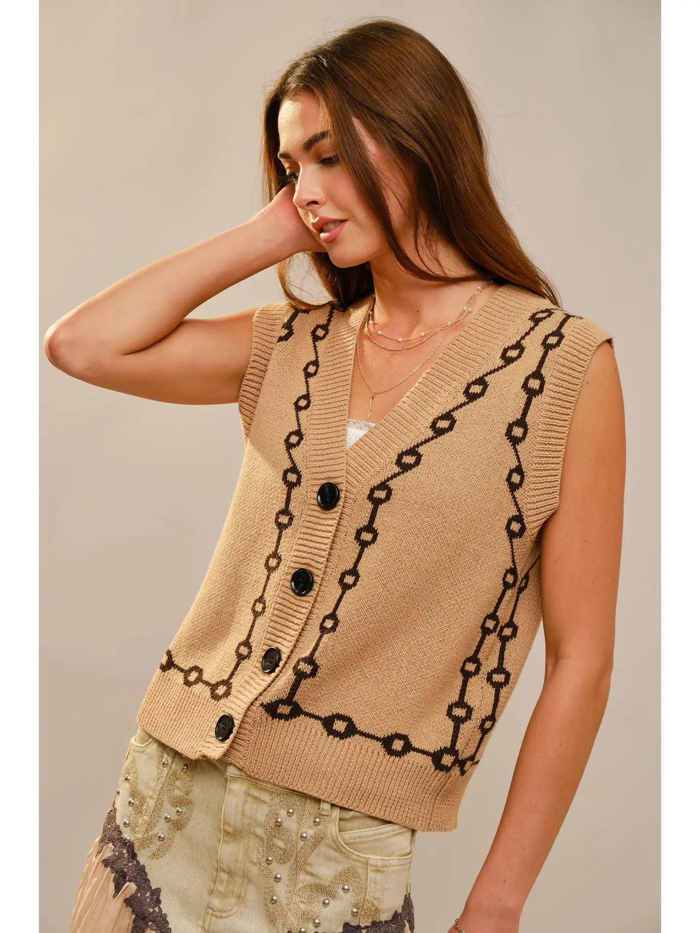 Woman wearing a beige knit vest with brown chain design on a plain background