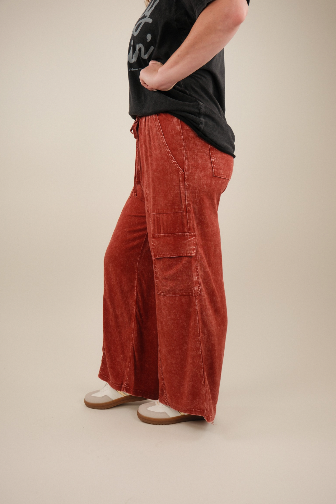 Person wearing rust-colored wide-leg pants and a black t-shirt on a beige background