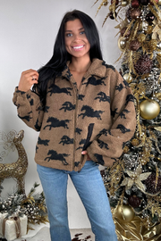 Woman wearing a brown fleece jacket with horse patterns in front of a decorated Christmas tree.