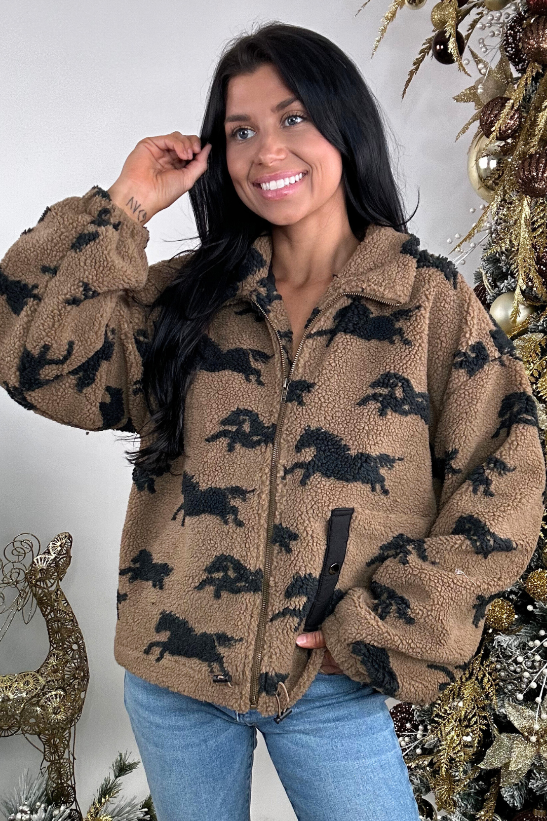 Woman wearing a brown fleece jacket with horse patterns in front of a decorated Christmas tree.